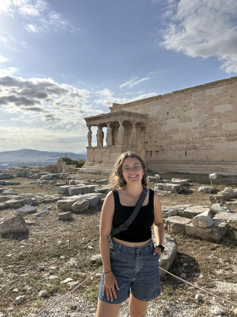 Young woman with brown hair and black tank top standing in front of the Erechtheion in Athens, Greece